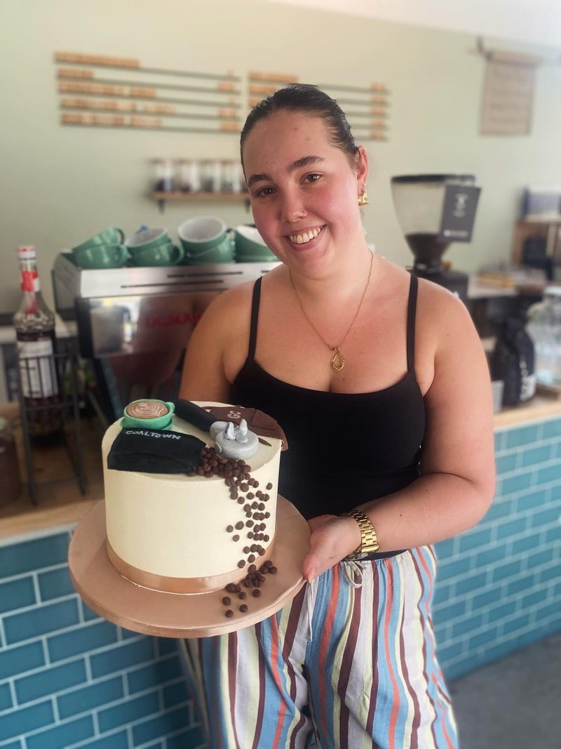 A member of the Ground Control team behind the counter holding a decorated celebration cake.