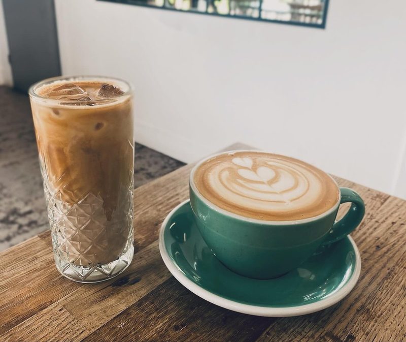 An iced latte in a cut-glass tumbler next to a hot latte.