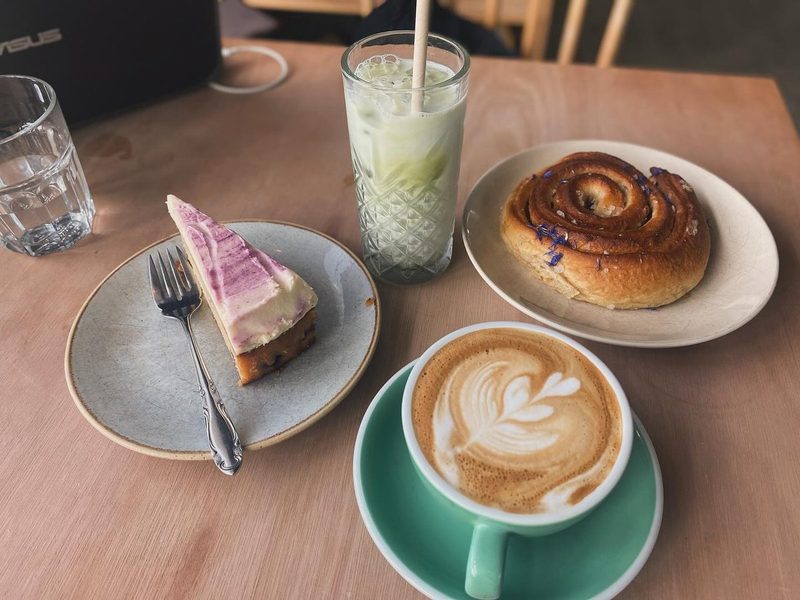 A table spread with a slice of cake, an iced matcha, a cinnamon bun and a latte.