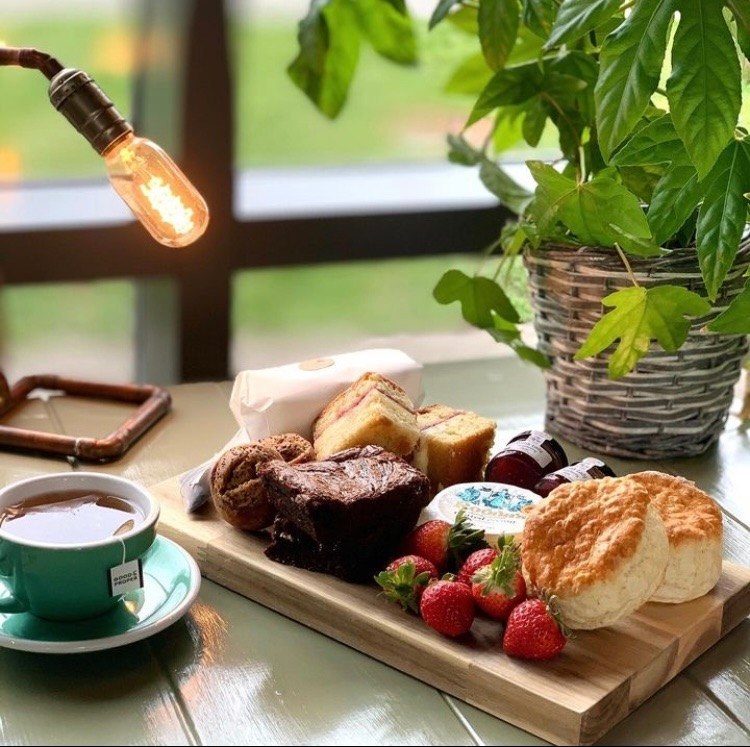 A wooden board of scones, brownies and strawberries with a cup of tea, by the window.